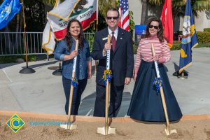 Howard Kummerman, Rachel Ghatikar and a young lady in a blue shirt and pants holding shovels in the dirt at VRC Groundbreaking.