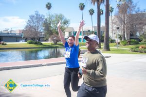 Smiling man running on campus and a woman in a blue t shirt with hands raised.