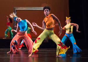 Dancers on stage wearing colorful pants and tops