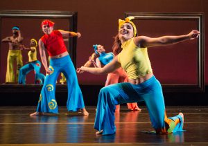 Dancers on stage wearing colorful pants and tops