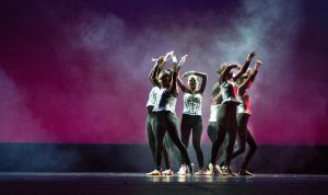 Dancers on stage wearing black pants and white corset tops