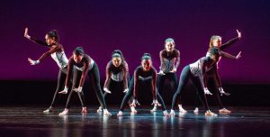 Dancers on stage wearing black pants and white corset tops