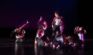 Dancers on stage wearing black pants and white corset tops