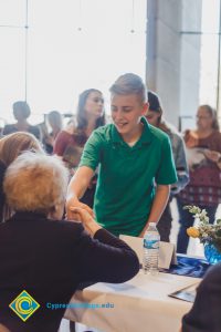 A young boy in a green polo shakes hands with an older woman who is seated.