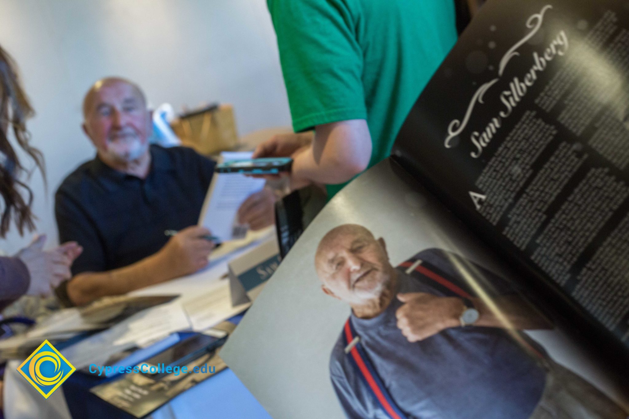 A program photo of Holocaust survivor Sam Silberbery is opened while Sam looks on in the background at the 2018 Yom HaShoah event.