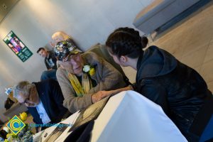 A young man in a black hoodie speaks to Holocaust survivor Gerda Seifer at 2018 Yom HaShoah event.