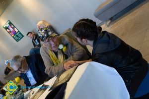 A young man in a black hoodie speaks to Holocaust survivor Gerda Seifer at 2018 Yom HaShoah event.