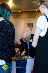 A man in a black suit signs a book for two women.