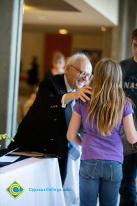 A Holocaust survivor with his hand on the shoulder of a young girl in a purple top and blue denim jeans.