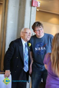A young man in glasses and a NASA t shirt, standing with a Holocaust survivor in a black suit and blue tie.