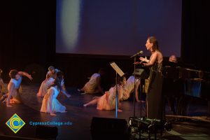 Woman at the microphone as dancers perform at the 2018 Yom HaShoah event.