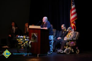 Gentleman speaks at the Yom HaShoah event while several guest look on.