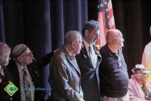 An older gentleman in a brown suit, a man in a kippah , Clifford Lester and another gentleman in tan khaki pants and a dark pullover standing on stage for the 2018 Yom HaShoah event.