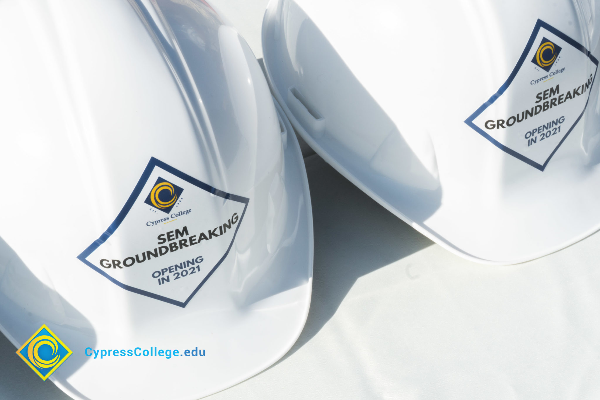 Rows of white hard hats with Cypress College SEM Groundbreaking stickers on the front.