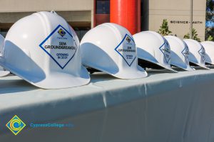 Rows of white hard hats with Cypress College SEM Groundbreaking stickers on the front.