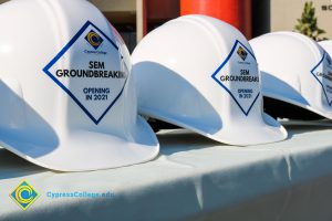 Rows of white hard hats with Cypress College SEM Groundbreaking stickers on the front.