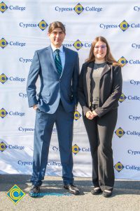 Young man with blue suit and tie with a young woman with glasses and long brown hair.