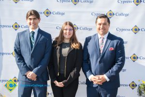 Two men with blue suits and tie with a young woman with glasses and long brown hair.