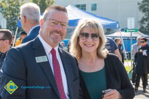 A man in a suit with red tie and woman wearing sunglasses and green shirt.