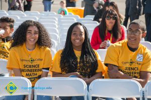 Four students wearing yellow Science, Engineering and Math shirts and Cari Jorgensen in the background.