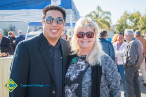Henry Hua with a blond woman wearing sunglasses and black and white floral blouse.