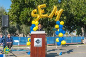 Dr. Schilling at podium with blue and yellow balloon arch and SEM balloons.