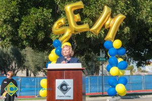 Dr. Cheryl Marshall at podium with blue and yellow balloon arch and SEM balloons.