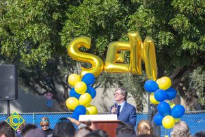 Richard Fee speaking to audience at SEM Groundbreaking ceremony with blue and gold balloons in the background.