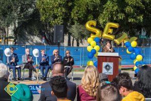 Young lady with long brown hair and glasses speaking to audience at SEM Groundbreaking ceremony.