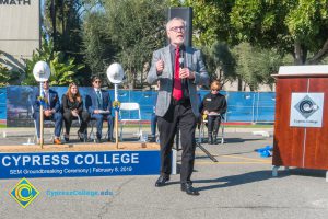 Man in suit and red tie speaking at SEM Groundbreaking ceremony.