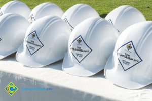 Rows of white hard hats with Cypress College SEM Groundbreaking stickers on the front.