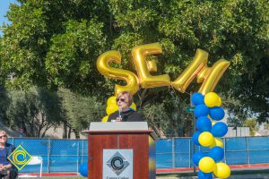 Dr. Schilling at podium with blue and yellow balloon arch and SEM balloons.