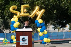 Dr. Schilling at podium with blue and yellow balloon arch and SEM balloons.