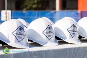 Rows of white hard hats with Cypress College SEM Groundbreaking stickers on the front.