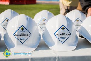 Rows of white hard hats with Cypress College SEM Groundbreaking stickers on the front.