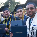 Smiling graduates during commencement holding degree.