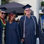 Four graduates in cap and gown smiling.