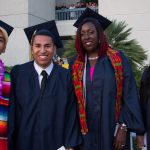 Four smiling graduates in full regalia.