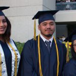 Three graduates in cap and gown smiling at commencement.