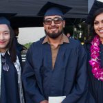 Three smiling graduates in cap and gown.