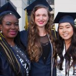 Three smiling graduates in cap and gown.