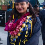 A STEM student smiling in her cap and gown and wearing several floral leis.