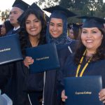 A group of happy graduates posing with their degrees at commencement.