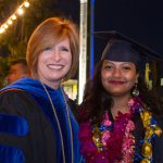 Dr. JoAnna Schilling with a smiling graduate after commencement with the lighted campanile in the background.