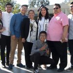 A graduate wearing her cap and gown and displaying the EOPS stole, surrounded by her family.