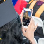 Graduate taking a photo of stage during commencement.