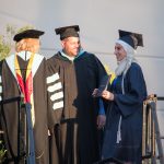 Dr. Schilling, a faculty member and a student in full graduation regalia on stage during commencement.