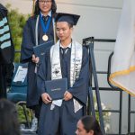 Young man in cap and gown holding his degree during commencement.