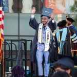 Young man holding up his degree and waving during commencement.