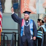 Young man holding up his degree during commencement.